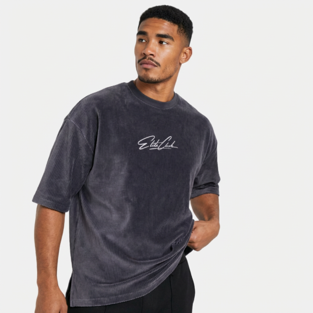 Athletischer Mann trägt Elite Club Cord T-Shirt in Anthrazit, seitliche Pose mit Blick zur Seite, schwarzer Hose, cleanes Studio Setting