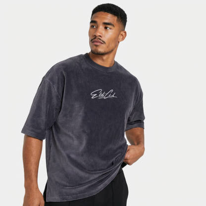 Athletischer Mann trägt Elite Club Cord T-Shirt in Anthrazit, seitliche Pose mit Blick zur Seite, schwarzer Hose, cleanes Studio Setting