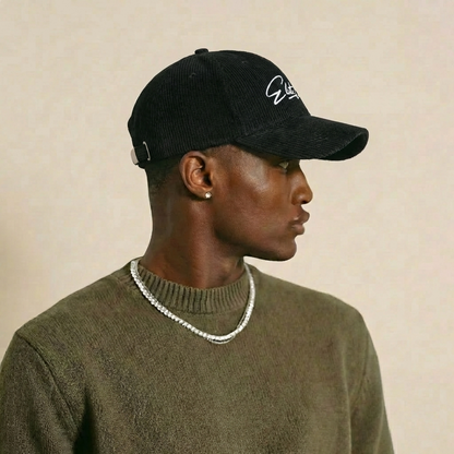 Schwarze Elite Club Cord Basecap mit weißem Logo Stick, strukturierte Cord Oberfläche, gebogener Schirm, Produktaufnahme vor neutralem Hintergrund.